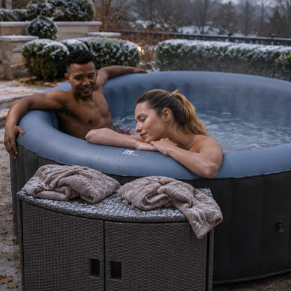 Two people relaxing in a Bergen MSpa hot tub outdoors with a Wicker Cabinet Round during cold winter day - portable sps NZ